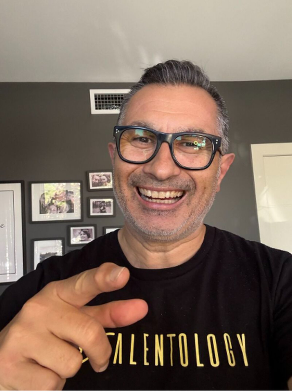 Trevor Churchley grinning at the camera at home and pointing at the Talentology logo on his black T-shirt